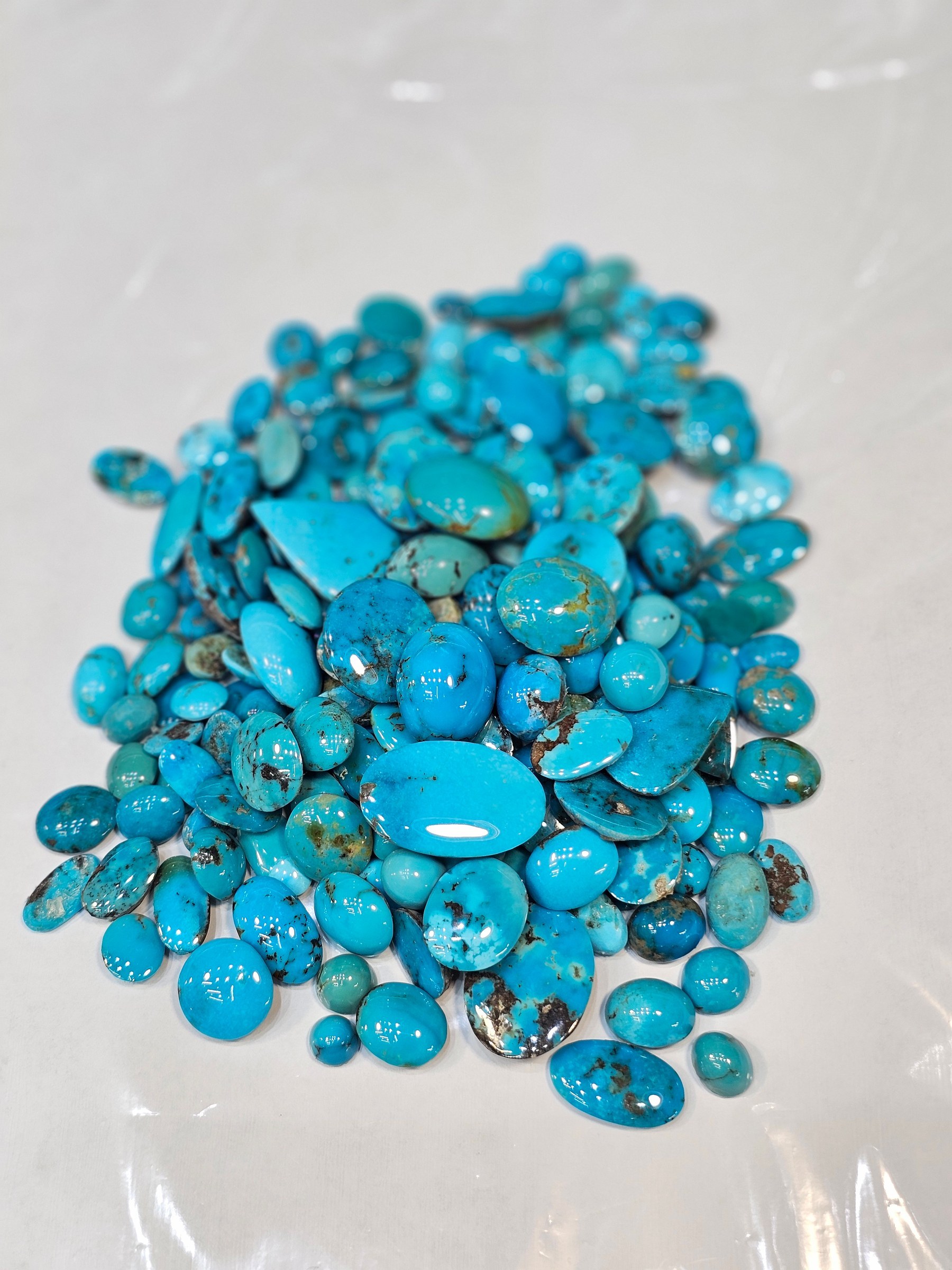 A pile of loose polished turquoise cabochons in brighter blue and brown matrix on a white sheet.