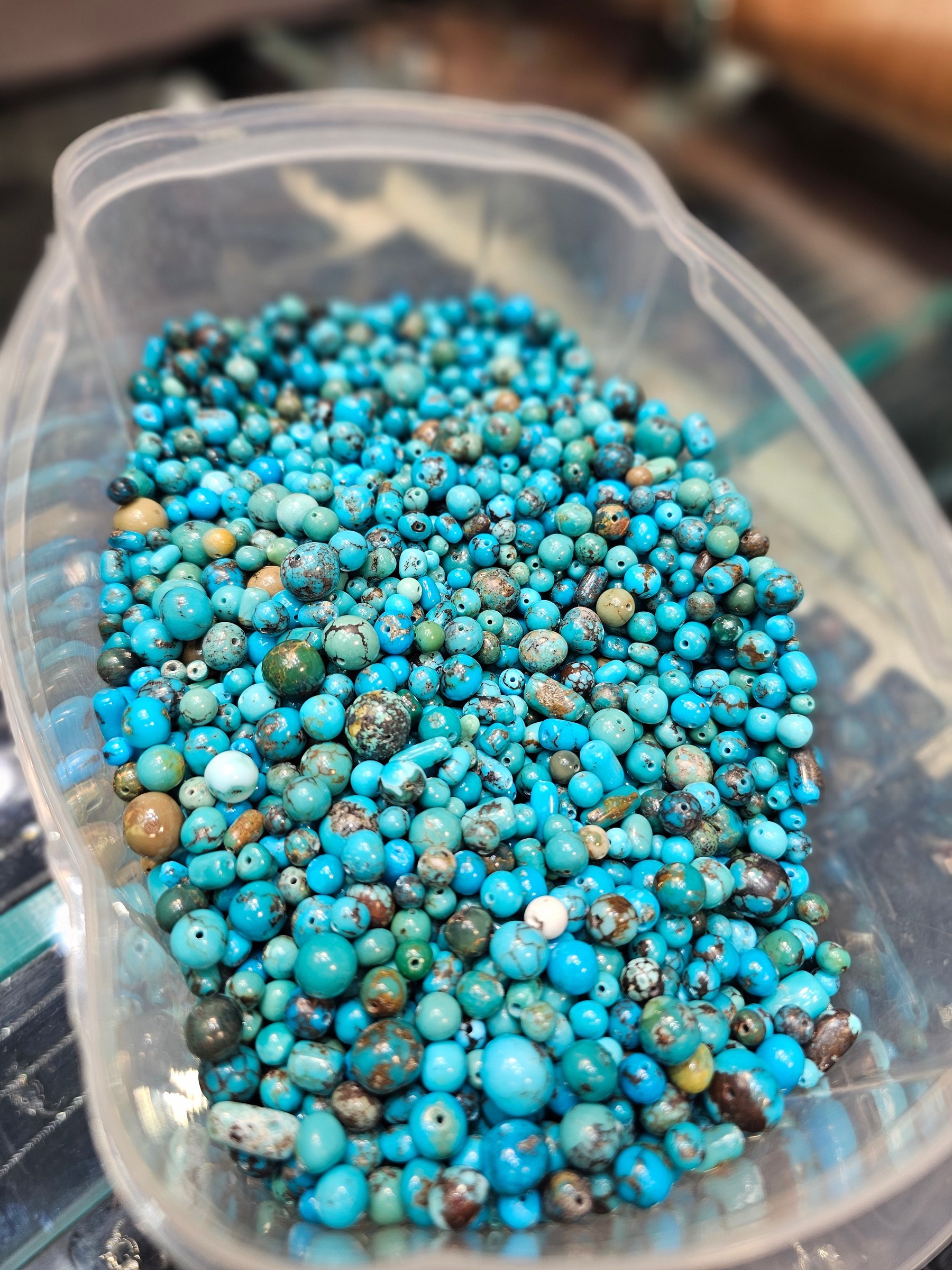 A plastic tub filled with round drilled turquoise beads in blue with brown and green matrix.